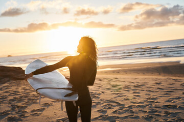 Fototapeta na wymiar Warm shot of surfer woman holding SUP board while walking at the beach before training