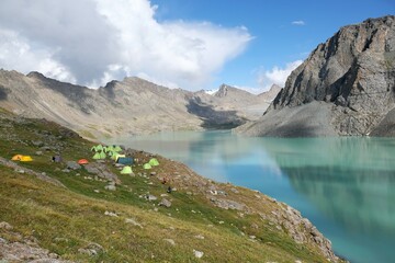 Colorful tents on bank of Lake Ala-Köl (Ala-kol, Ala-kul) in Tien Shan mountains in west of Kyrgyzstan, Asia. Cyan color of lake under steep mountaines. Touristic destination for trekking.