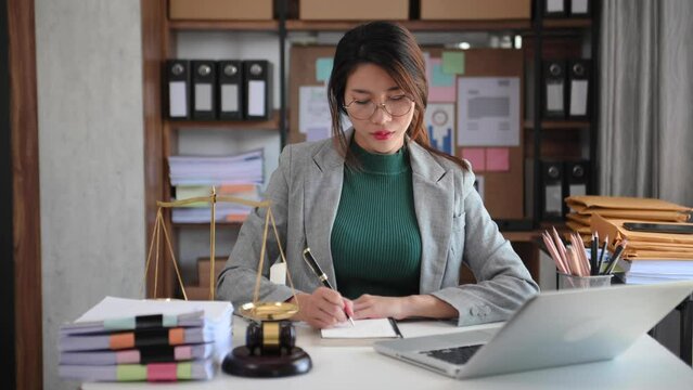 justice and law concept. asian woman lawyer working and judge in a courtroom  the gavel, working with smart phone and laptop and digital tablet computer on wood table