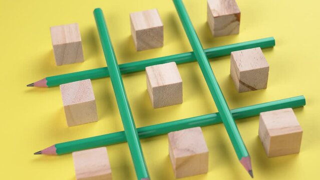 Business strategy concept. Creative game with pencils and wooden cubes on a bright yellow background. The hand sets the block in the center of the structure