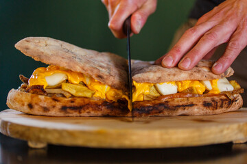 Panuozzo napoletano cotto nel forno a legna con patate al forno, porchetta, provola e cheddar fuso mentre viene tagliato a metà con un coltello da cucina