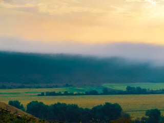 Morning fog over the fields in the valley. A plain under gentle hills. Atmospheric landscape.