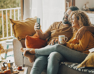 Happy adult couple at home enjoy mobile phone connection doing video call conference with friends or parents away. Technology lifestyle indoor house