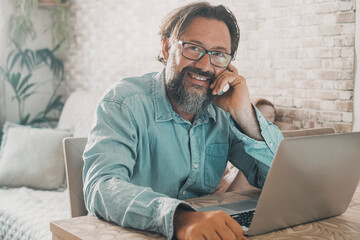 Portrait of cheerful man smiling and looking on camera with computer on the table. Adult young male...