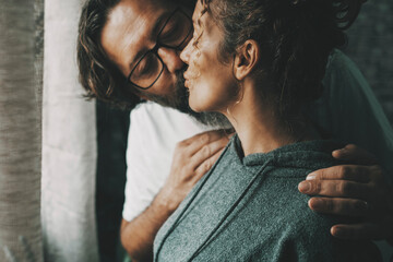 Romantic adult couple kissing with tenderness and sweetness at home in indoor leisure love activity. Relationship concept and marriage lifestyle people. Man kiss woman in the dark with window light