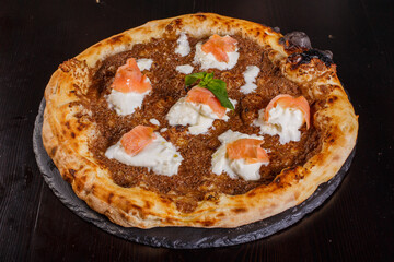 Pizza gourmet napoletana con patè di olive nere, stracciata di bufala e salmone affumicato servita in una pizzeria