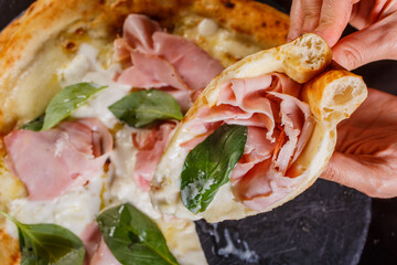 Fetta di pizza napoletana gourmet con prosciutto cotto, mozzarella, basilico fresco e stracciata di bufala appena tagliata da una cliente