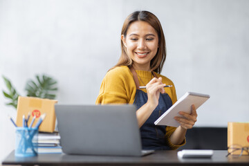 Fototapeta premium Asian woman look like india girl working SME business at workplace at home. use laptop checking customer order online shipping boxes, freelance SME entrepreneur online business idea.