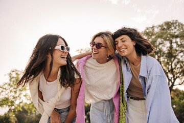 Cute young caucasian women enjoy spending time together outdoors summer. Brunettes, blonde wear casual clothes, sunglasses. Leisure concept