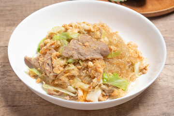 Stir fried vermicelli with pork, egg and collard greens in a white plate.