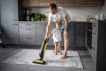 Father and daughter having fun with vacuum cleaner while cleaning at home kitchen
