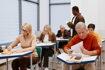 Group of senior people making notes at desks while teacher reading a lecture during training in class
