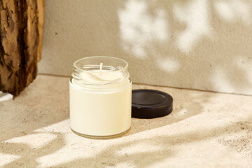 Simple composition with aromatic burning candle in jar. Mockup soy wax candle with wick in natural...