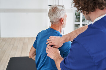 Fototapeta Manual therapist massaging shoulder blades of elderly male during the treatment obraz