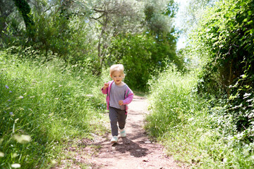 Naklejka na ściany i meble Little girl walking along the path in the park. High quality photo