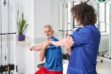 Fototapeta premium Skilful young specialist showing how to stretching hands to his mature patient