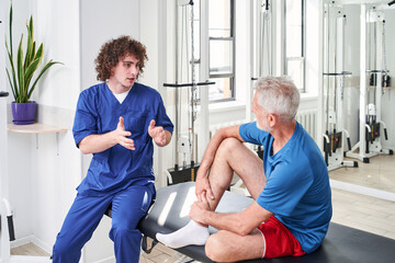 Physical therapist emotionally gesturing while chatting with his senior patient