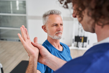 Chiropractor giving help to senior man with arm pain for physical recovery