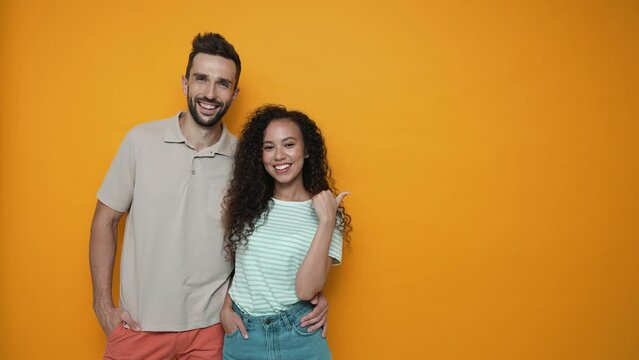 Pretty brunette couple pointing finger to the copyspace and looking at the camera in the yellow studio