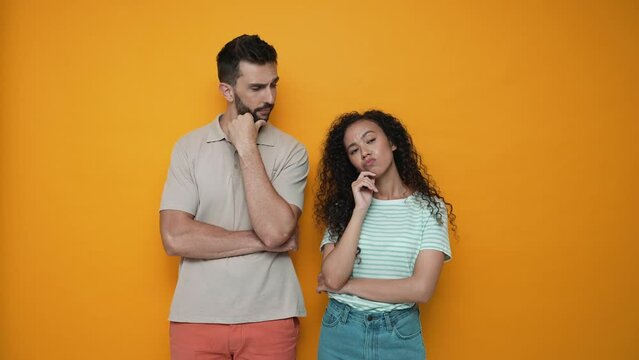 Pensive brunette couple thinking about something while standing in the yellow studio