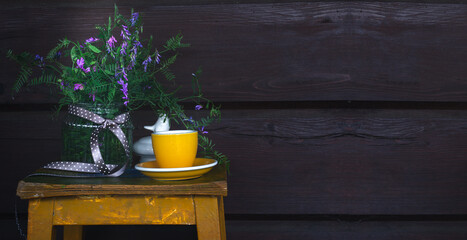 A stack of books, a cup, a bouquet of wild flowers against the background of a dark wooden wall of a country house. Summer relax background. Slow life
