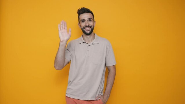 Smiling brunet man wearing t-shirt greeting at the camera in the yellow studio