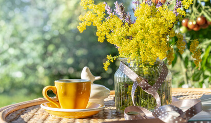 Yellow cup with coffee or tea, a bouquet of wild flowers on the terrace of a country wooden house. Rest, relax in the summer, vacation