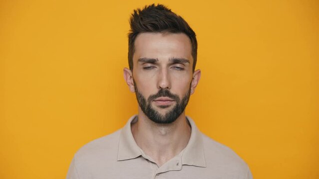 Concentrated brunet man wearing t-shirt opening eyes at the camera in the yellow studio