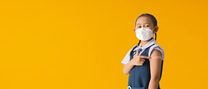 Back to school banner idea concept, Asian student little girl showing pointing with finger to bandage on her arm shoulder wearing protective mask done with vaccinations