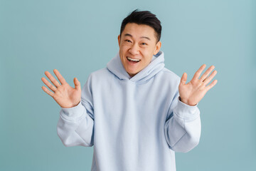 Young asian man wearing hoodie gesturing and laughing at camera
