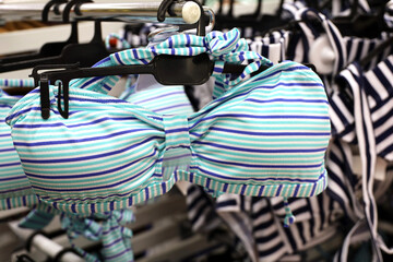 Fototapeta na wymiar Striped swimsuits hanging on rack in lingerie store, selective focus. Female fashion for beach vacation