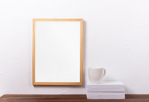 White frame mockup hanging on the wall with stack of books and coffee cup