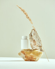 Stone podium with white plastic mockup jar, dry plant. Dietary supplements, vitamins, cosmetics...