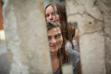 Two pretty girlfriends are reflected in a street mirror on the wall.