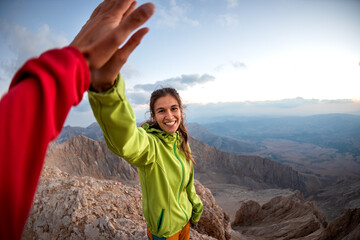 A woman with a backpack climbed to the top of the mountain and gives a high five..