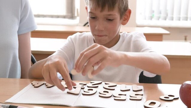 The child and the teacher do math, lay out wooden numbers on the table. A mother helps her son learn to count. The babysitter helps to complete school assignments. back to school