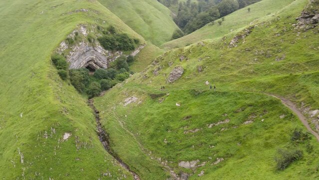 People on the fresh green pathway walking toward the mouth of the Arpea Cave.