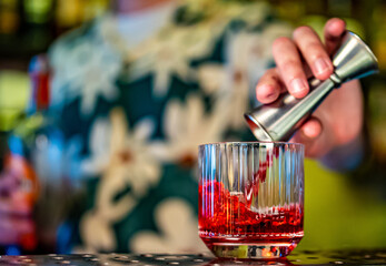 bartender pours red campari drink from jigger into glass in bar
