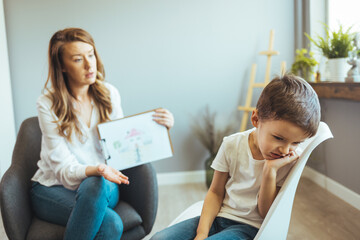 Young Boy Talking With Counselor At Home. Female psychologist working with little boy in office. Young female school psychologist having serious conversation with smart little boy