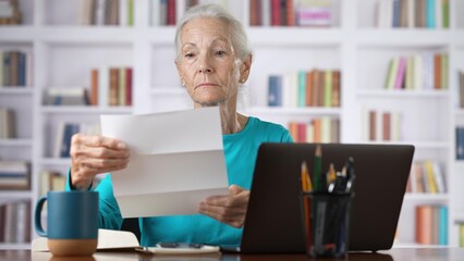 Stressed senior woman holding letter troubled with domestic bills, bad news.