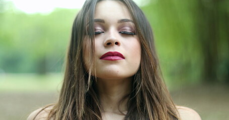 Girl in her 20s taking a deep breath. Young woman breathing the fresh air at park looking to camera feeling refreshed and happy