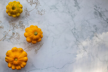 Autumn, fall background with yellow pattypan scallop squash vegetable and flowers on white marble table. Top view, flat lay, copy space. 	