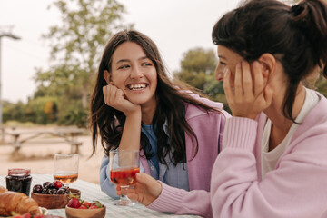 Nice young caucasian women laugh relaxing over glass of wine in nature outside city. Brunettes wear cardigans in warm weather. Lifestyle, different emotions, leisure concept.
