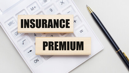Wooden blocks with the INSURANCE PREMIUM Iie on a light background on a white calculator. Nearby is a black handle. Business concept