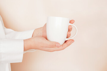 Woman hands holding mock up white cup, mug close-up on beige background. Blank template, logo, text design, promotional, text message.
