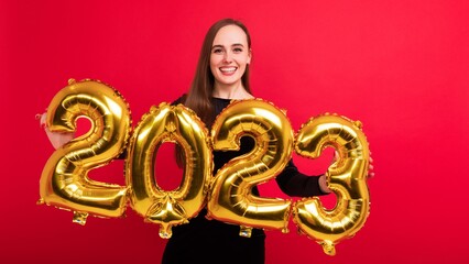 Portrait of a young brunette woman holding the numbers of the new year 2023 on a red background