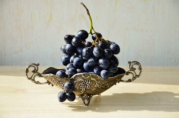 Still life with dark grapes in a silver vase on a light background.