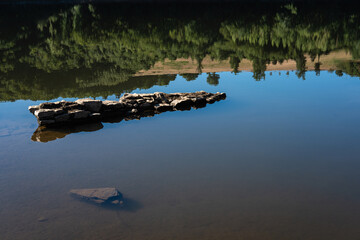 Reflets des arbres d'une forêt sur un lac avec un mur en pierre dans l'eau.
