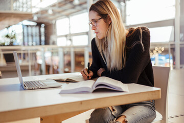 Focused young caucasian woman studying at desk in university library