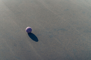 Pelota de tenis morada en el suelo con sombra reflejada en el suelo